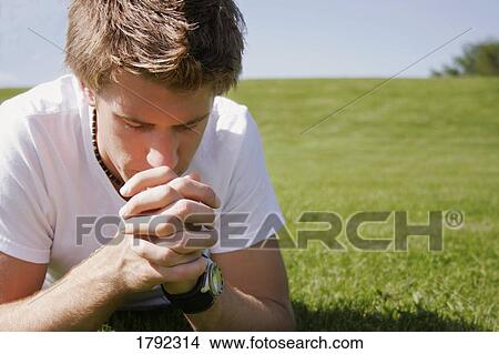 Picture - Young man praying outside. Fotosearch