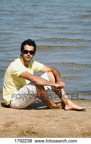 Stock Photo - Young man sitting on beach. Fotosearch