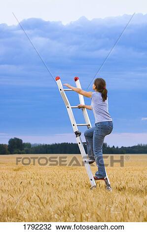 Stock Image - Young woman climbing ladder to heaven. Fotosearch