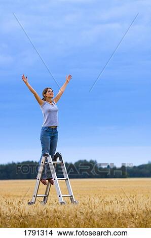 Picture - Young woman reaching to heaven from ladder in field. Fotosearch
