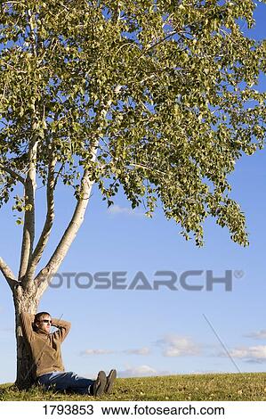 Stock Image - Man sitting under tree. Fotosearch