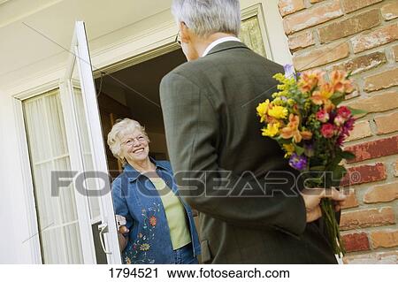 Stock Image - Man surprising a woman with flowers. Fotosearch