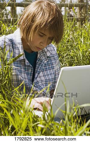 Stock Photography - Teen using laptop in tall grass. Fotosearch