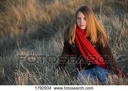 Teenage girl wearing a red scarf sitting in a grass field View Large Photo Image Picture - Teenage girl wearing a red scarf sitting in a grass field. Fotosearch