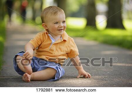 Stock Image - Toddler sits on sidewalk with bare feet. Fotosearch