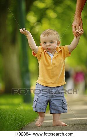 Toddler walking down sidewalk with bare feet while holding adult's hand View Large Photo Image Picture - Toddler walking down sidewalk with bare feet while holding adult's hand. Fotosearch