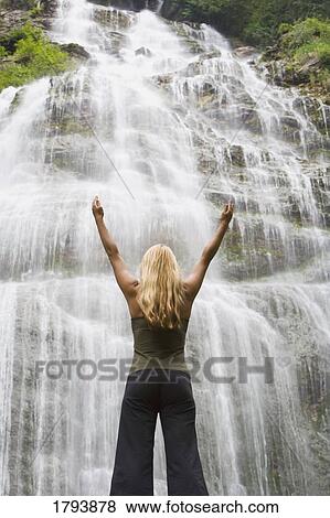 Woman with arms raised at the foot of a waterfall View Large Photo Image Stock Photo - Woman with arms raised at the foot of a waterfall. Fotosearch