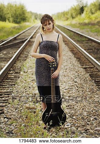 Stock Image - Young woman holding acoustic guitar on train tracks. Fotosearch