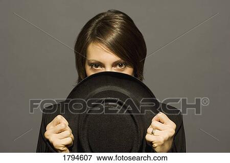 Stock Photo - Young woman holding hat in front of face. Fotosearch