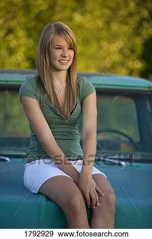 Stock Photo - Young woman sits on hood of old truck. Fotosearch