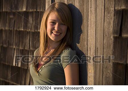 Picture - Young woman stands against old wooden building. Fotosearch