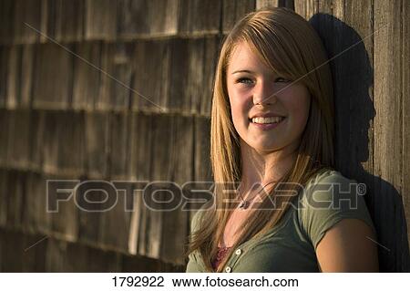 Stock Image - Young woman stands against old wooden building. Fotosearch
