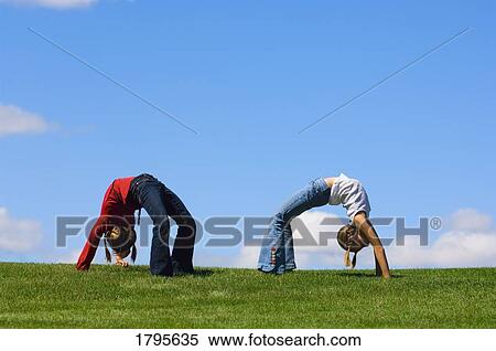 Two girls doing back arches on the grass View Large Photo Image Stock Photography - Two girls doing back arches on the grass. Fotosearch