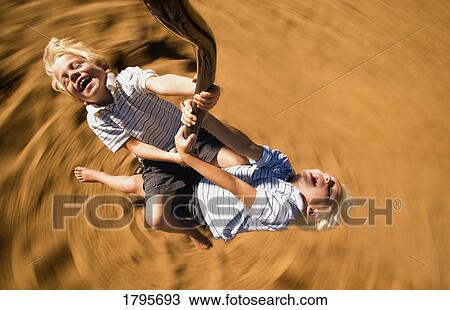 Stock Image - Boys spinning on playground ride. Fotosearch