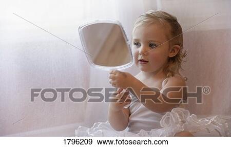Stock Photo - Little girl looking at herself in a hand mirror. Fotosearch