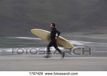 Stock Photo - A surfer running to the water with his board. Fotosearch