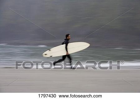 Stock Image - A surfer, running with board along the shoreline. Fotosearch