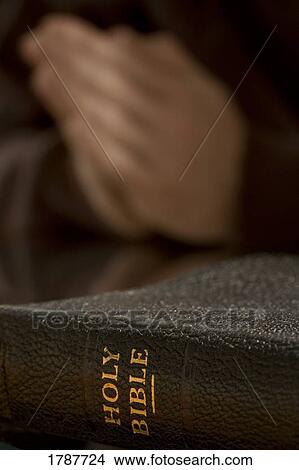 Picture - Bible with praying hands in background. Fotosearch