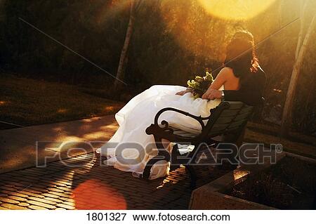 Stock Photo - Bride and groom sitting on bench with sun going down. Fotosearch