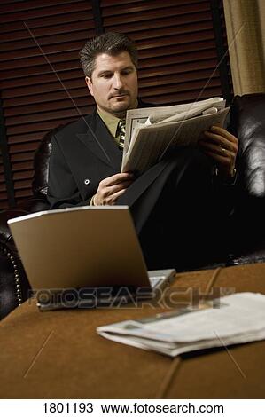 Businessman reading the newspaper with his laptop View Large Photo Image Stock Image - Businessman reading the newspaper with his laptop. Fotosearch