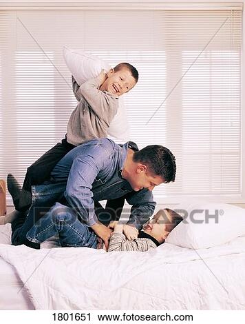 Stock Image - Dad and sons having pillow fight. Fotosearch