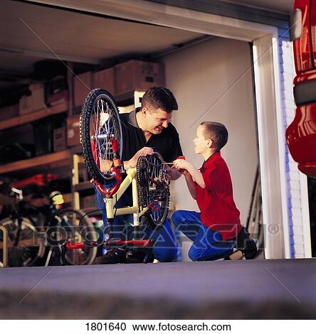 Stock Image - Father and son working on bike together. Fotosearch