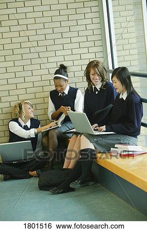 Stock Photograph - Four females in uniforms working on laptops in school hallway. Fotosearch