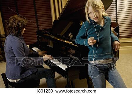 Girl listening to music while another plays piano View Large Photo Image Stock Image - Girl listening to music while another plays piano. Fotosearch