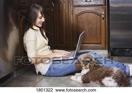 Stock Image - Girl working on laptop and sitting on the floor with dog. Fotosearch