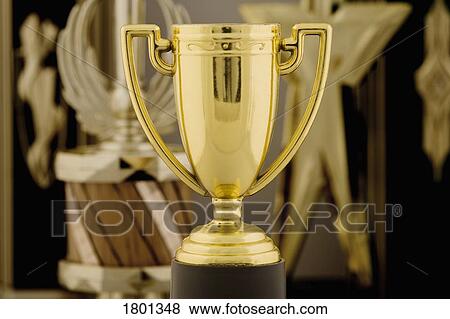 Stock Photo - Gold trophy cup with awards in background. Fotosearch