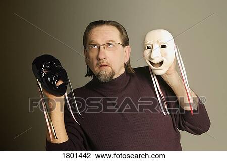 Stock Image - Man holding happy mask and sad mask. Fotosearch