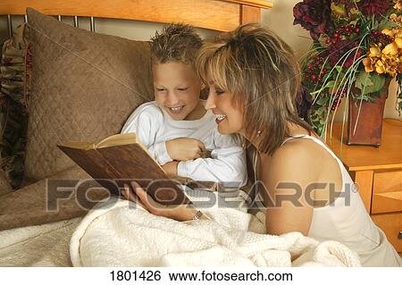 Stock Photograph - Mother and son reading together with mother beside the bed. Fotosearch