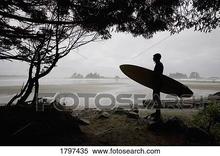 Stock Photography - Silhouette of a surfer looking out to the water from the beach. Fotosearch