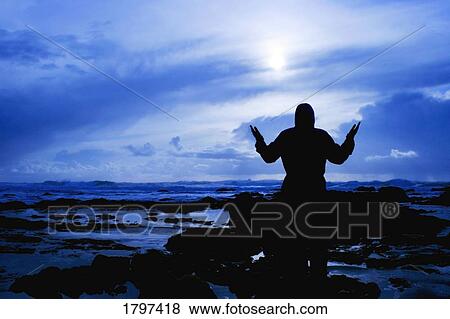 Silhouetted figure of someone worshipping by the ocean View Large Photo Image Stock Photo - Silhouetted figure of someone worshipping by the ocean. Fotosearch