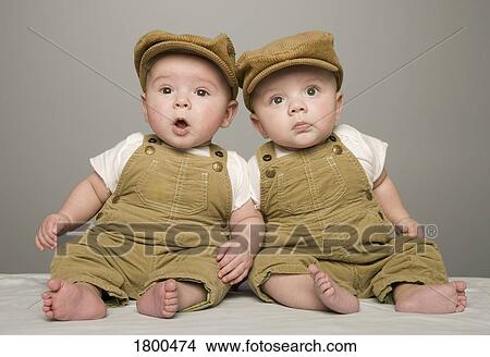 Picture - Two babies in matching hat and overalls. Fotosearch