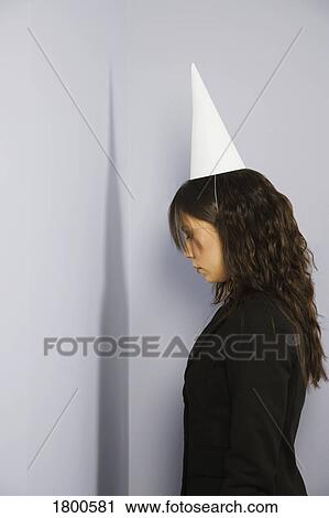 Stock Image - Woman facing corner with dunce cap. Fotosearch