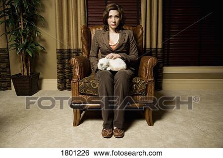 Stock Photograph - Woman holding cat sitting in chair. Fotosearch
