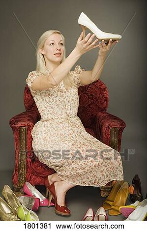 Woman holding up a shoe in the midst of many pairs of shoes View Large Photo Image Stock Image - Woman holding up a shoe in the midst of many pairs of shoes. Fotosearch