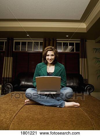 Stock Image - Woman working on laptop in living room. Fotosearch