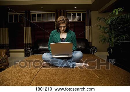 Stock Photo - Woman working on laptop in living room. Fotosearch
