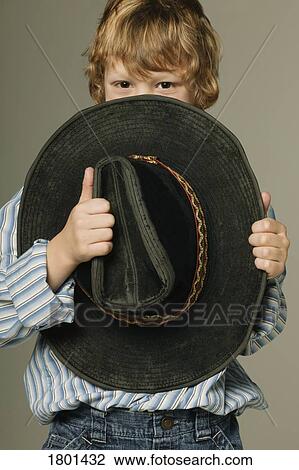 Stock Image - Young boy hiding part of face with large cowboy hat. Fotosearch