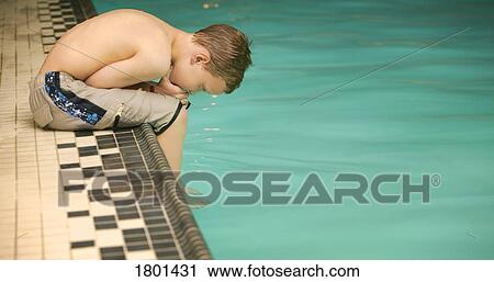Stock Image - Young boy sitting on edge of pool, leaning over. Fotosearch