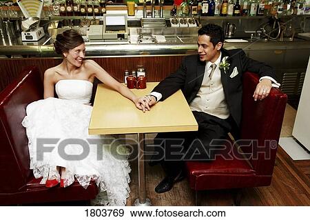 Stock Photo - A couple smiling and holding hands in a restaurant. Fotosearch