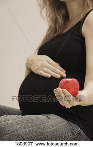 Stock Photo - A pregnant woman holding apple. Fotosearch