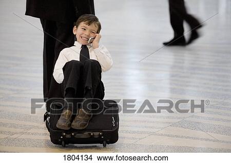 Picture - Boy riding on suitcase and talking on cell phone. Fotosearch