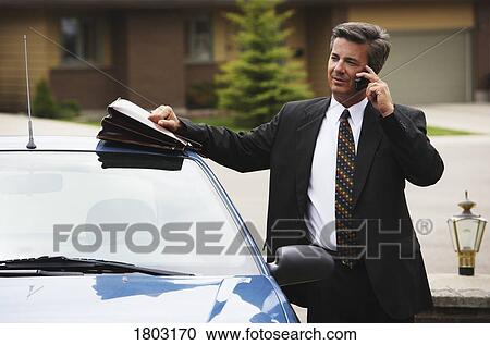 Stock Image - Businessman using mobile phone by car. Fotosearch