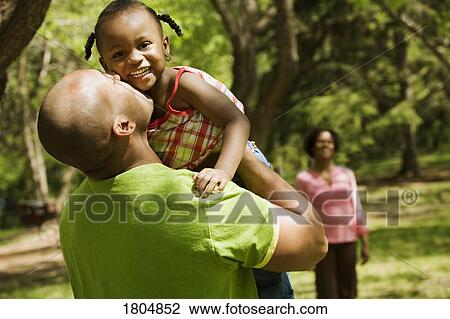 Father kissing daughter with mother in background View Large Photo Image Stock Image - Father kissing daughter with mother in background. Fotosearch