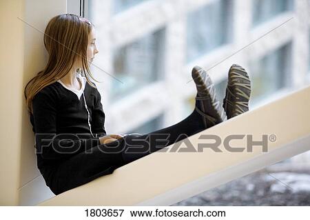 Stock Photo - Girl sitting on windowsill listening to music. Fotosearch