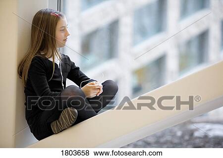 Stock Photo - Girl sitting on windowsill listening to music. Fotosearch