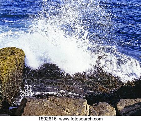 Stock Photograph - Large wave crashing on the rocks. Fotosearch
